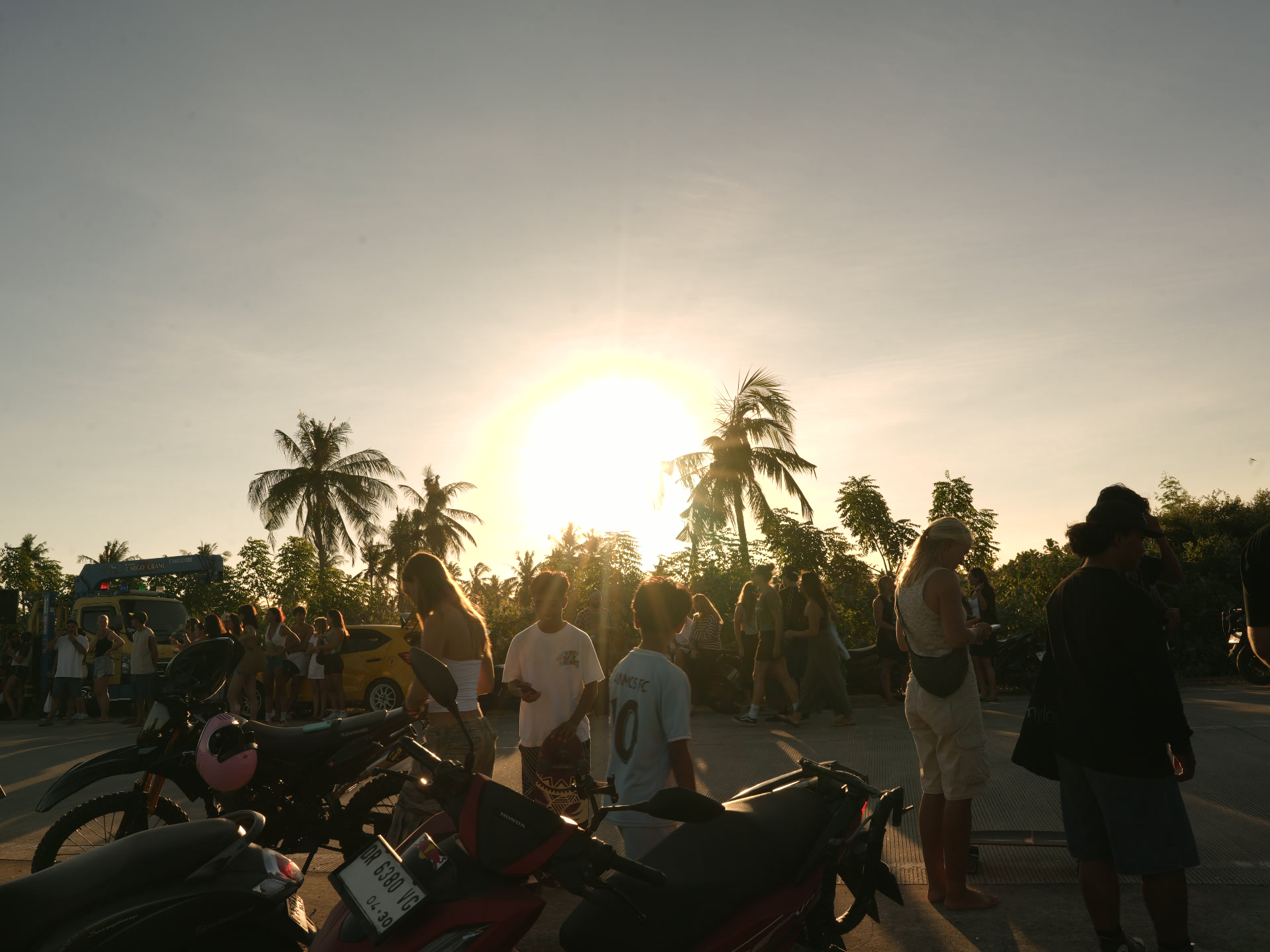 Sunset at a south Lombok beach road — visitors and scooters gathered under coconut palms