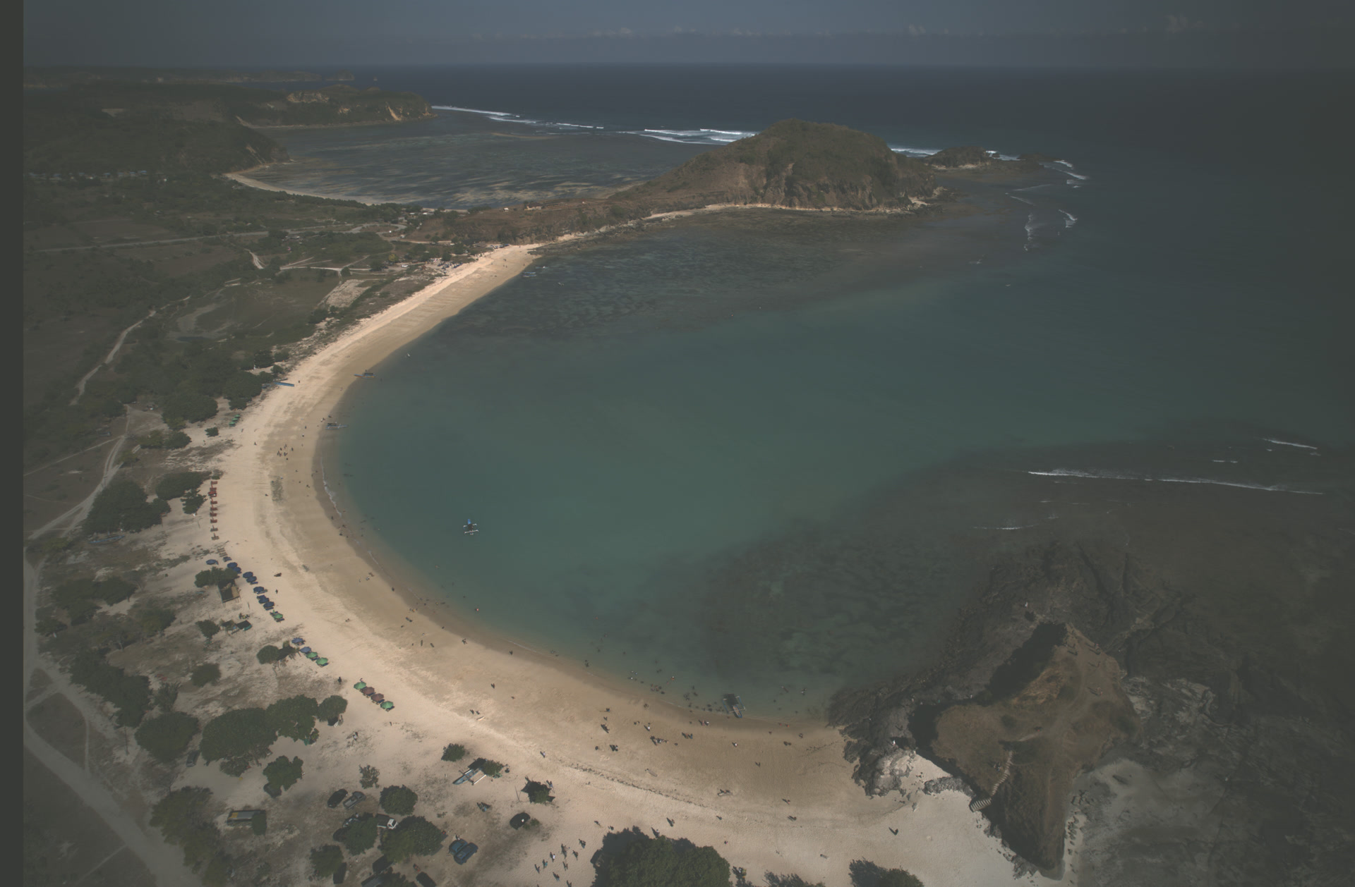 Aerial view of a crescent beach bay in South Lombok — turquoise water, white sand, and green headlands