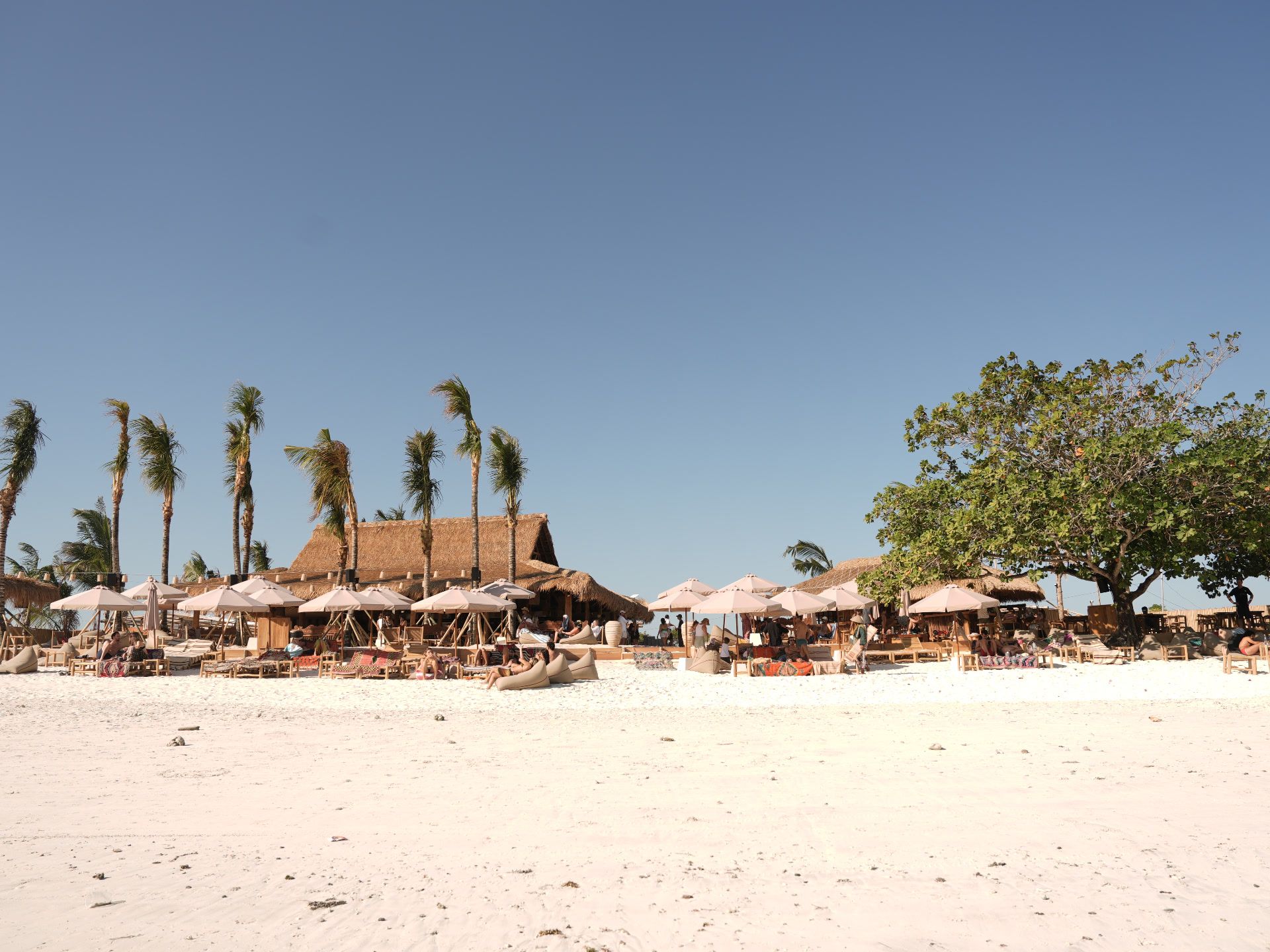 Beach club on the white sand of South Lombok — thatched roofs, palms, and umbrellas